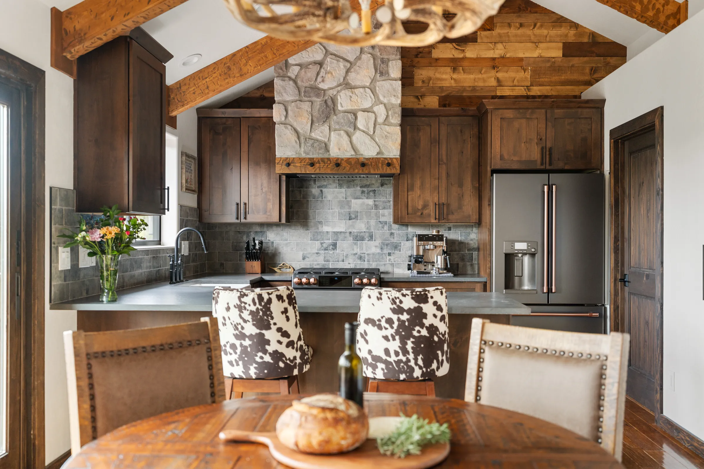 Remodeled kitchen with stone range hood beyond the dining table, Daybreak at Ponderosa, Refined Designs by Natalie