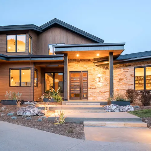 Custom mountain home entry at dusk with local stone and timber detailing, Refined Designs by Natalie